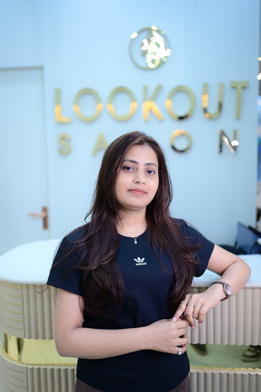 Woman in a dark T-shirt standing at the reception counter under the LookOut Salon sign