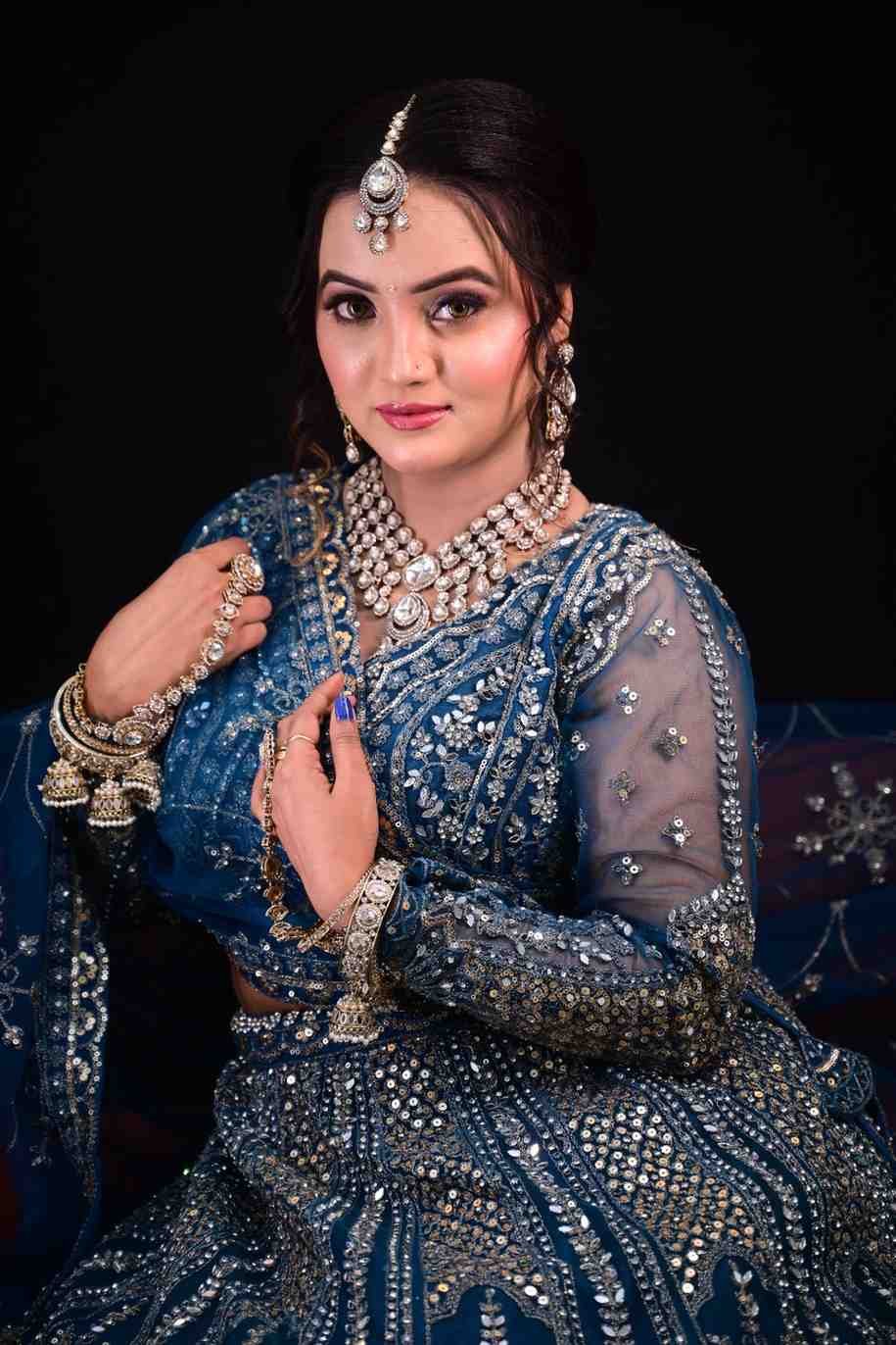 Bride in a blue embellished lehenga with layered necklaces against a dark background