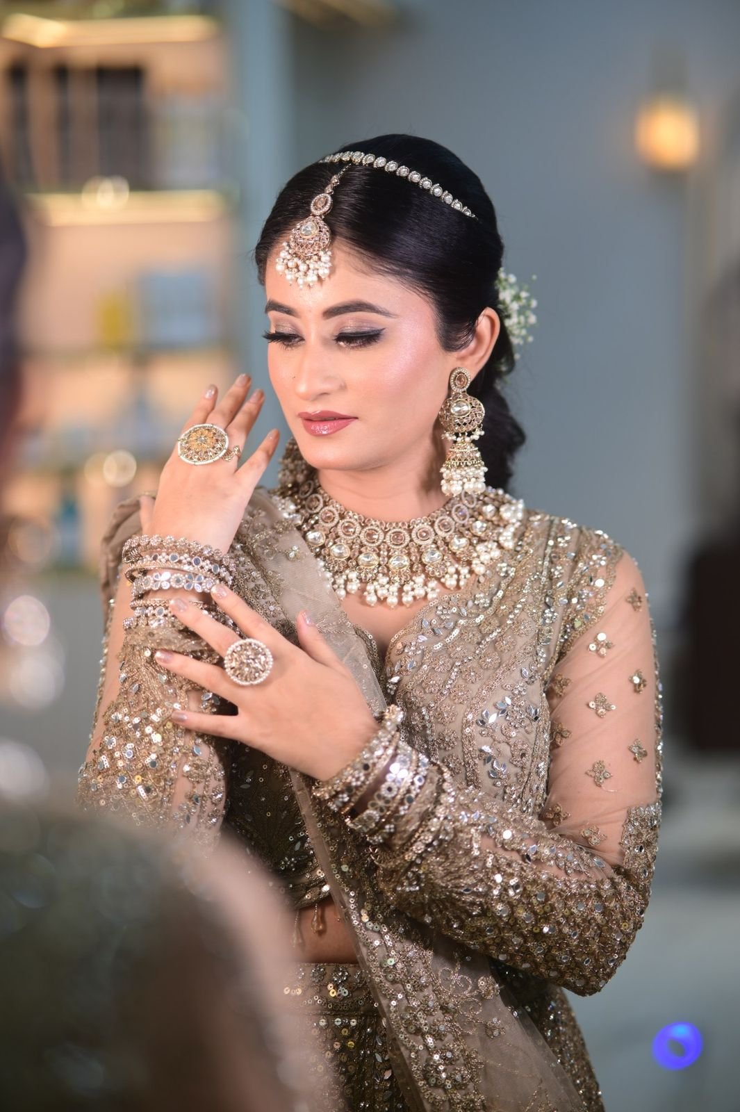 Bridal portrait with a hand raised to the cheek, wearing a champagne embroidered outfit, a layered necklace and a maang tikka