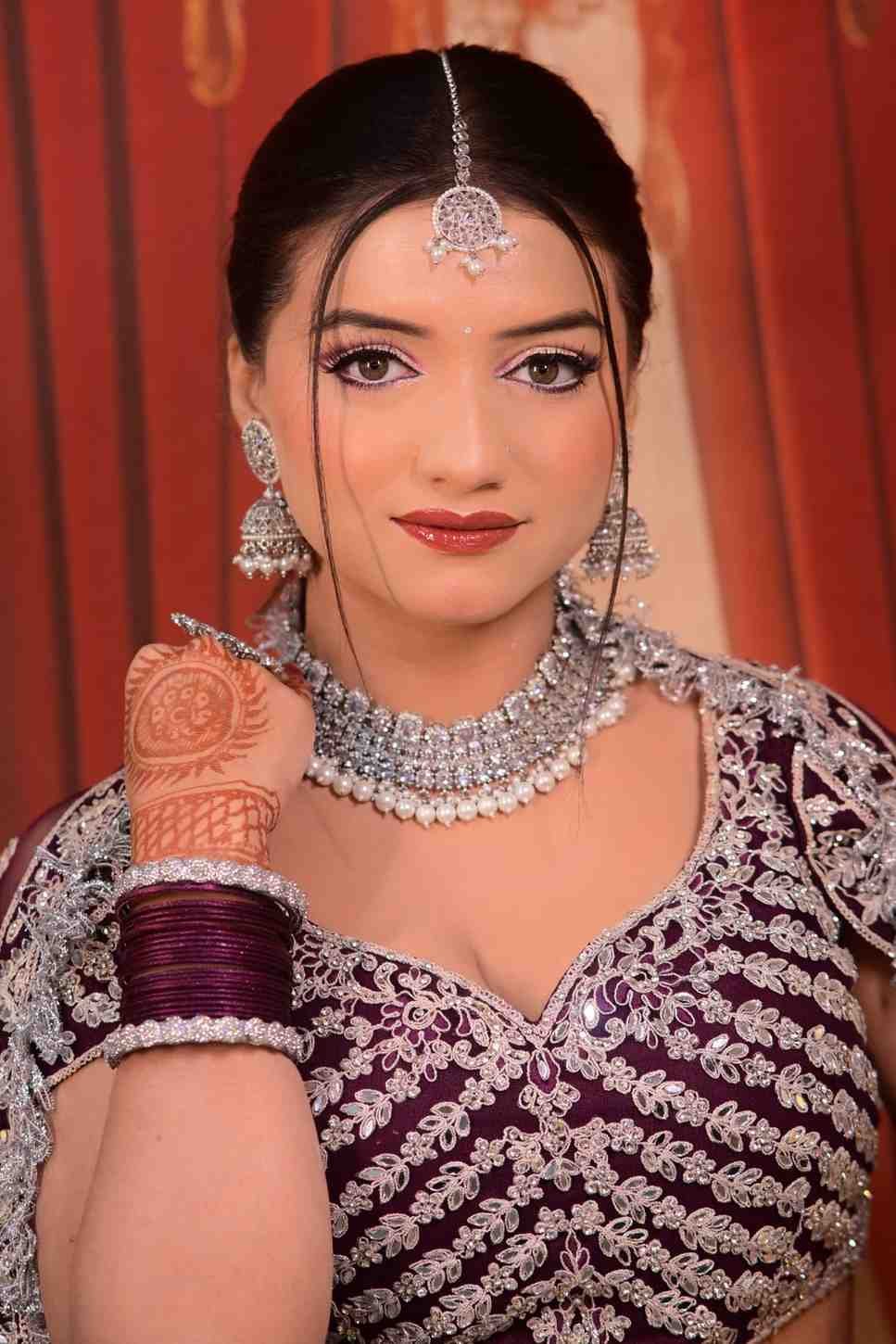 Close portrait of a bride in a maroon lehenga with a layered silver necklace and red bangles