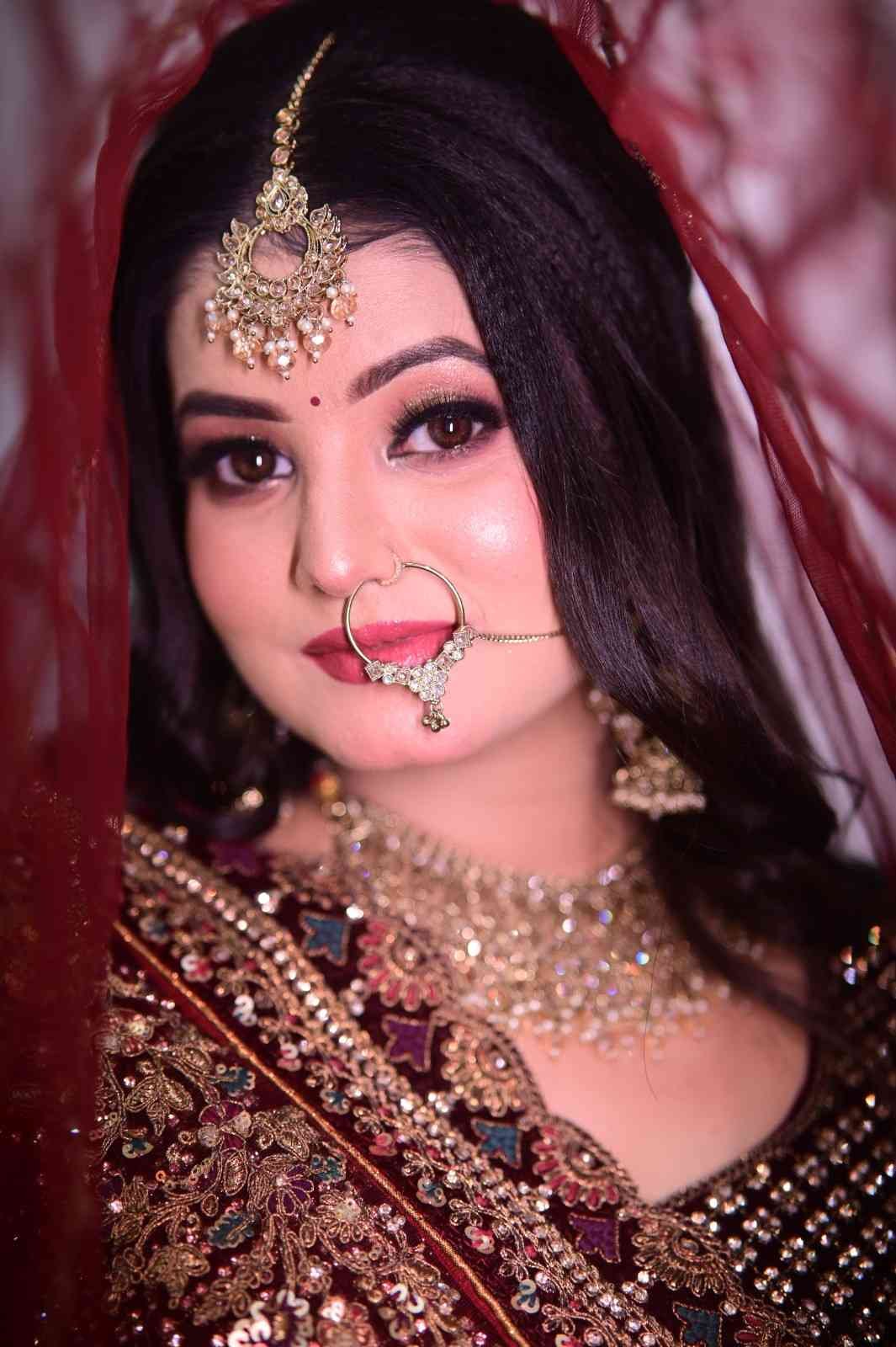 Bride in a dark maroon lehenga with a gold maang tikka and red veil