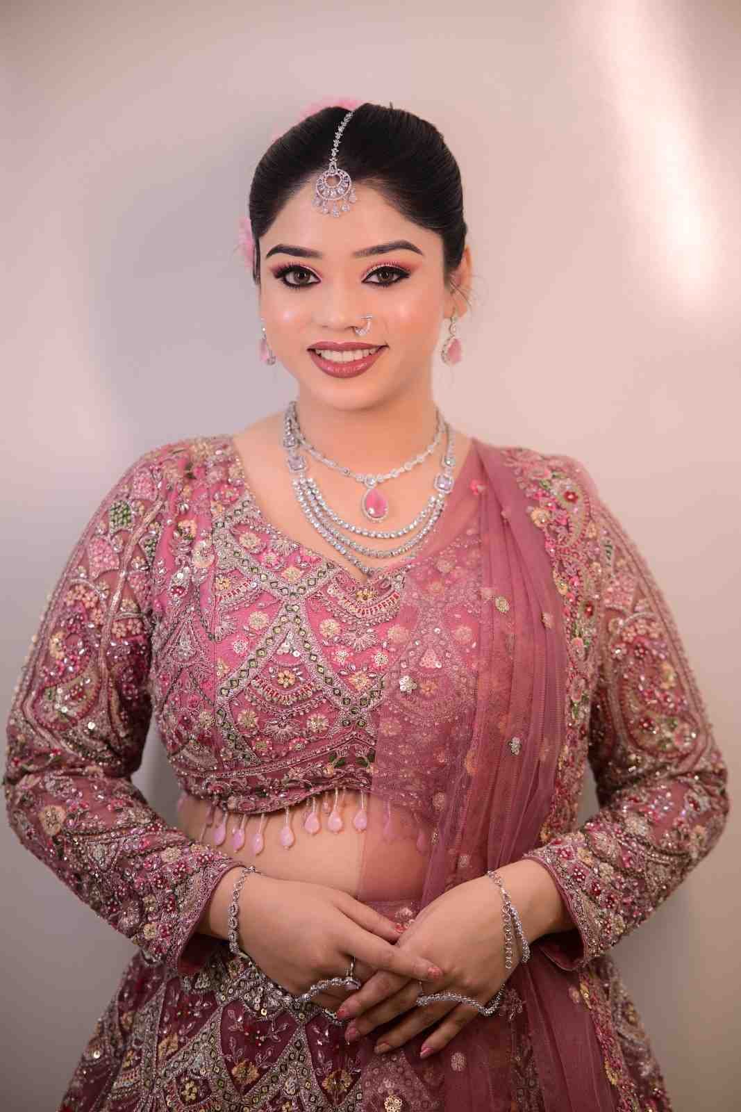 Bride in a pink embellished lehenga with a pearl necklace against a soft pink background
