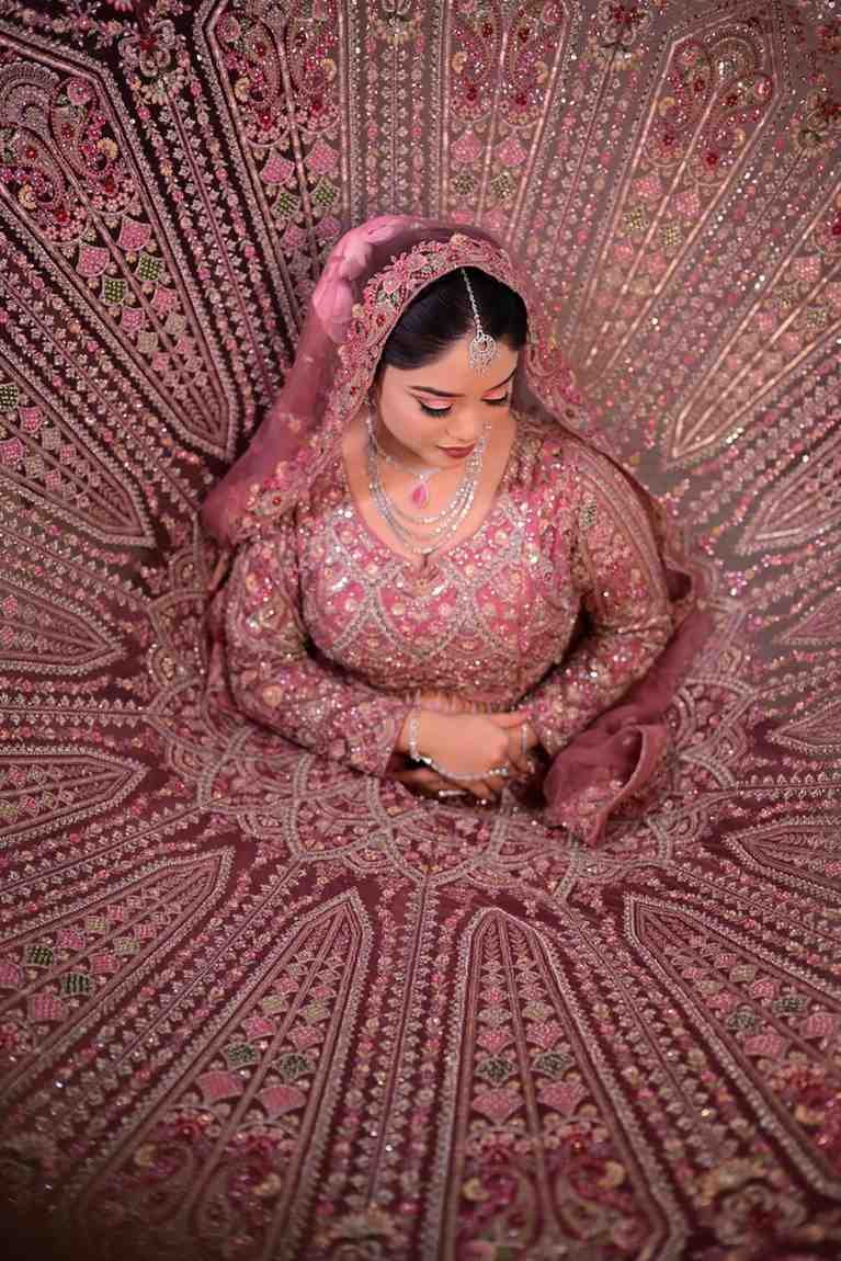 Overhead view of a bride in a pink lehenga seated with the skirt spread in a circle