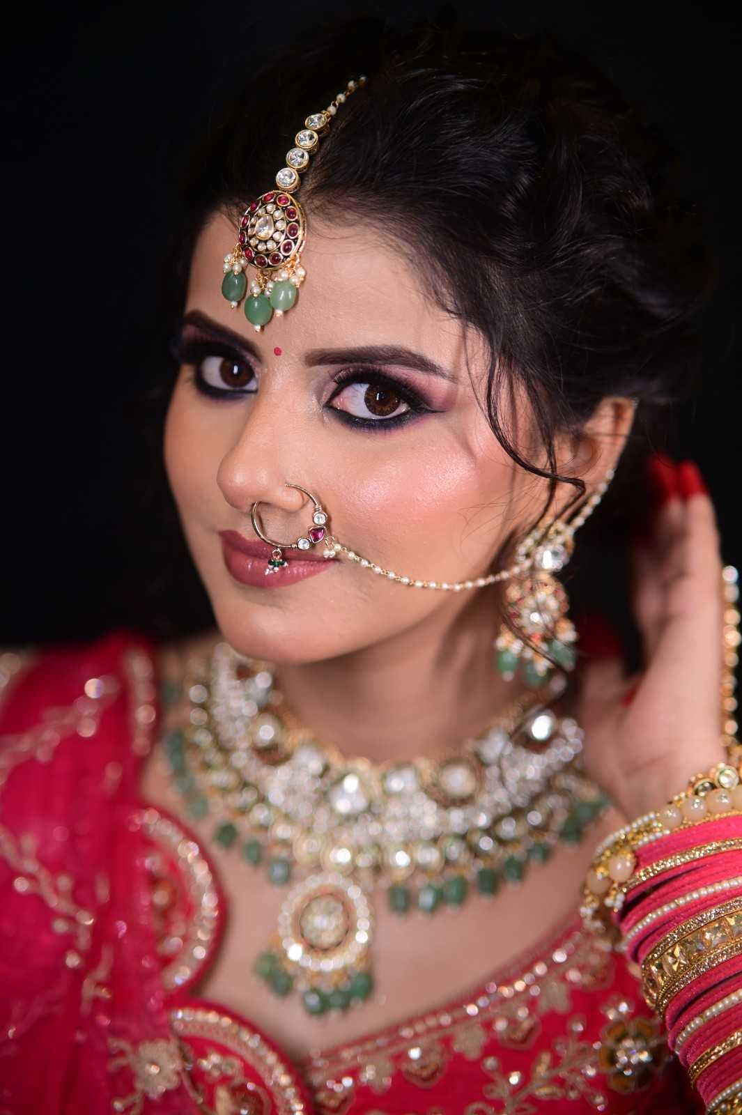 Bride in a red lehenga with a nath, maang tikka and green kundan necklace