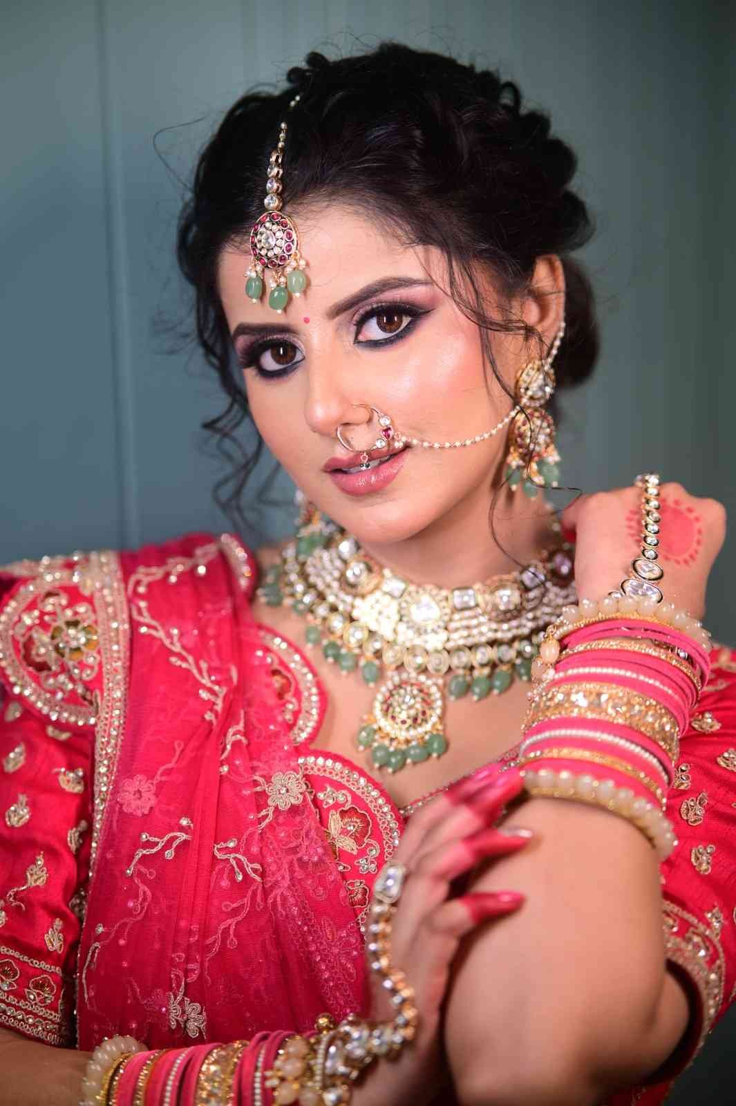 Bride in a red lehenga with a nose ring and maang tikka against a teal backdrop