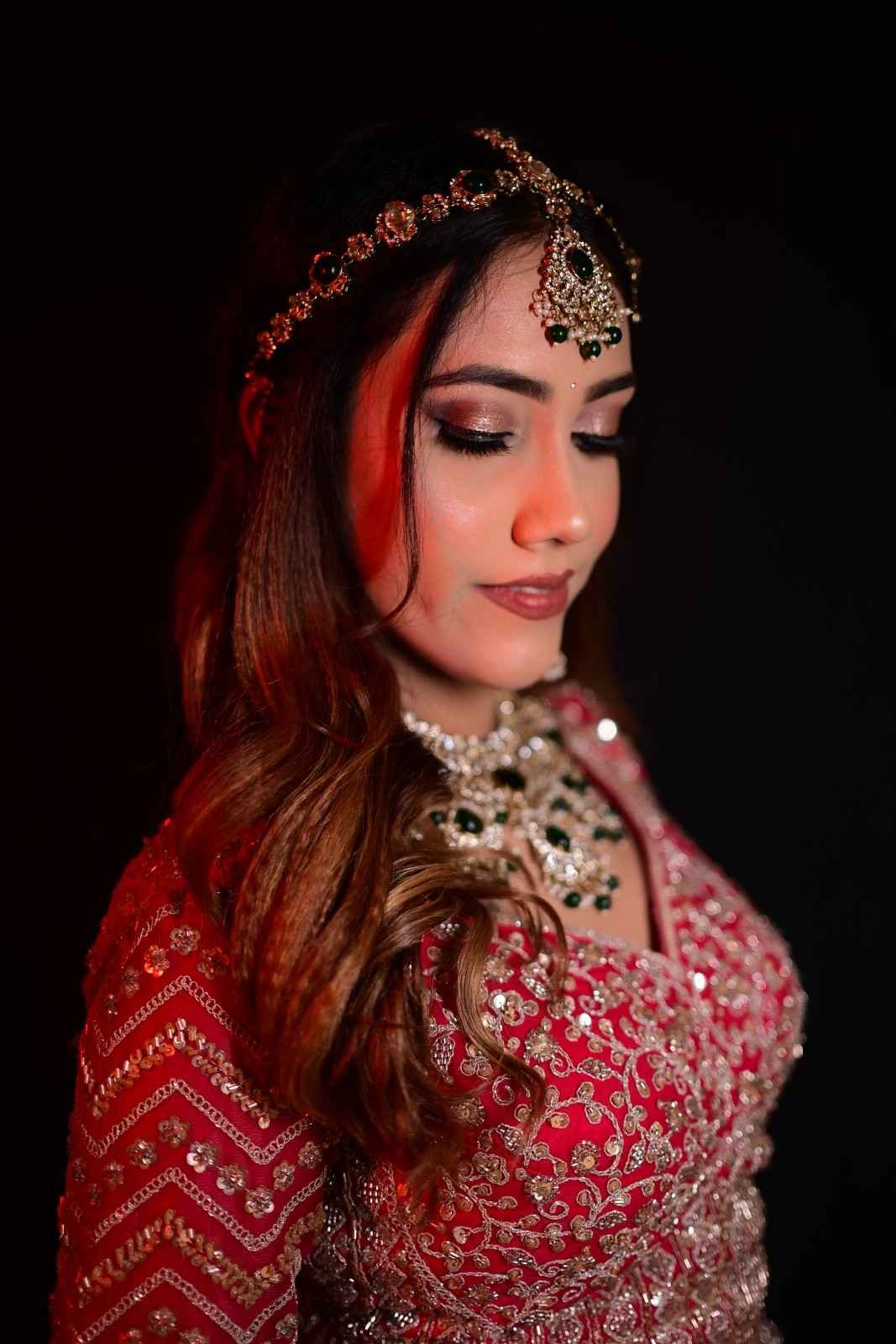 Bride with long loose waves and a head jewel, wearing a red lehenga against a dark background