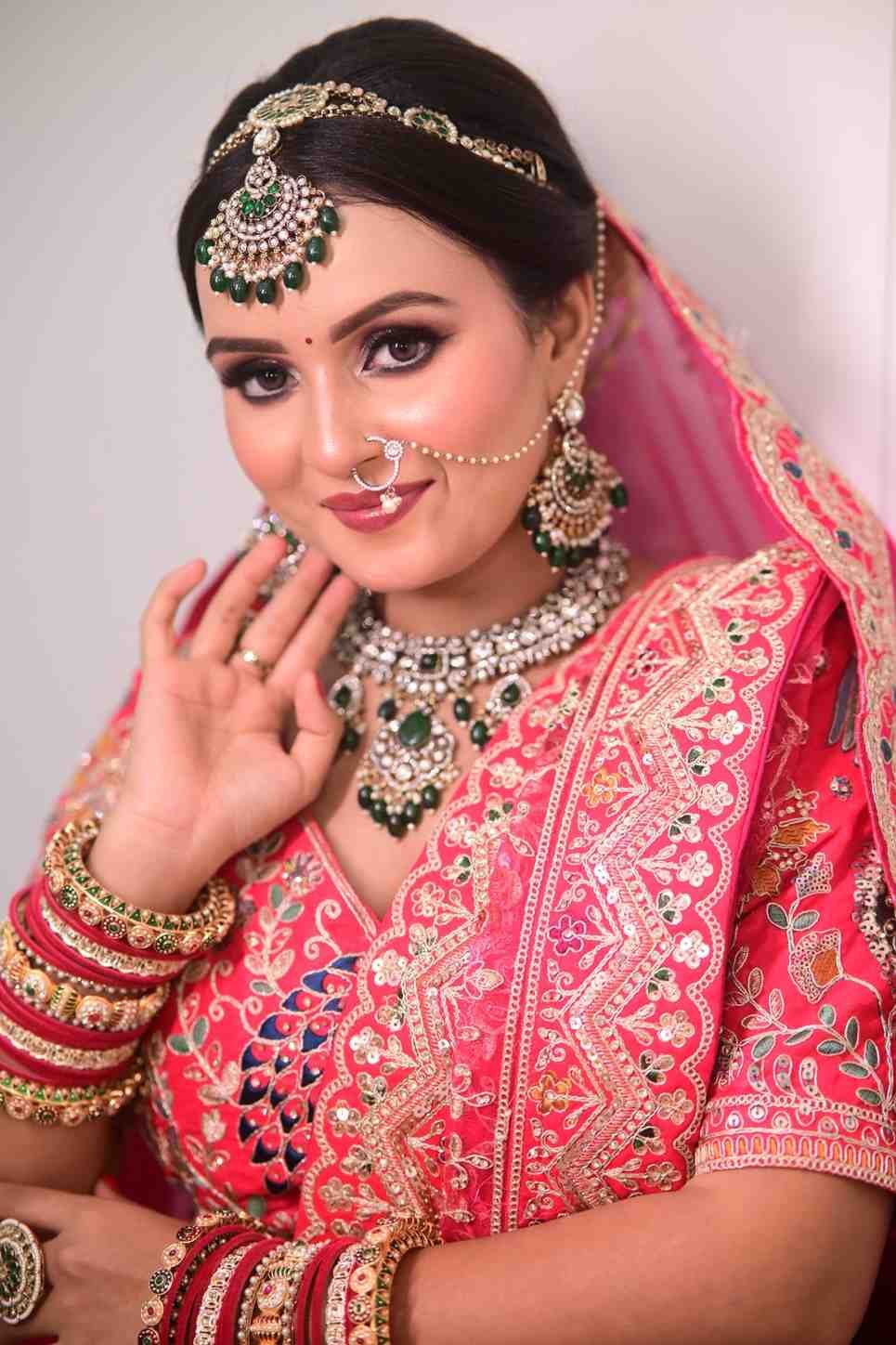 Bride in a red and gold embellished lehenga with a pink-red veil and kundan jewellery