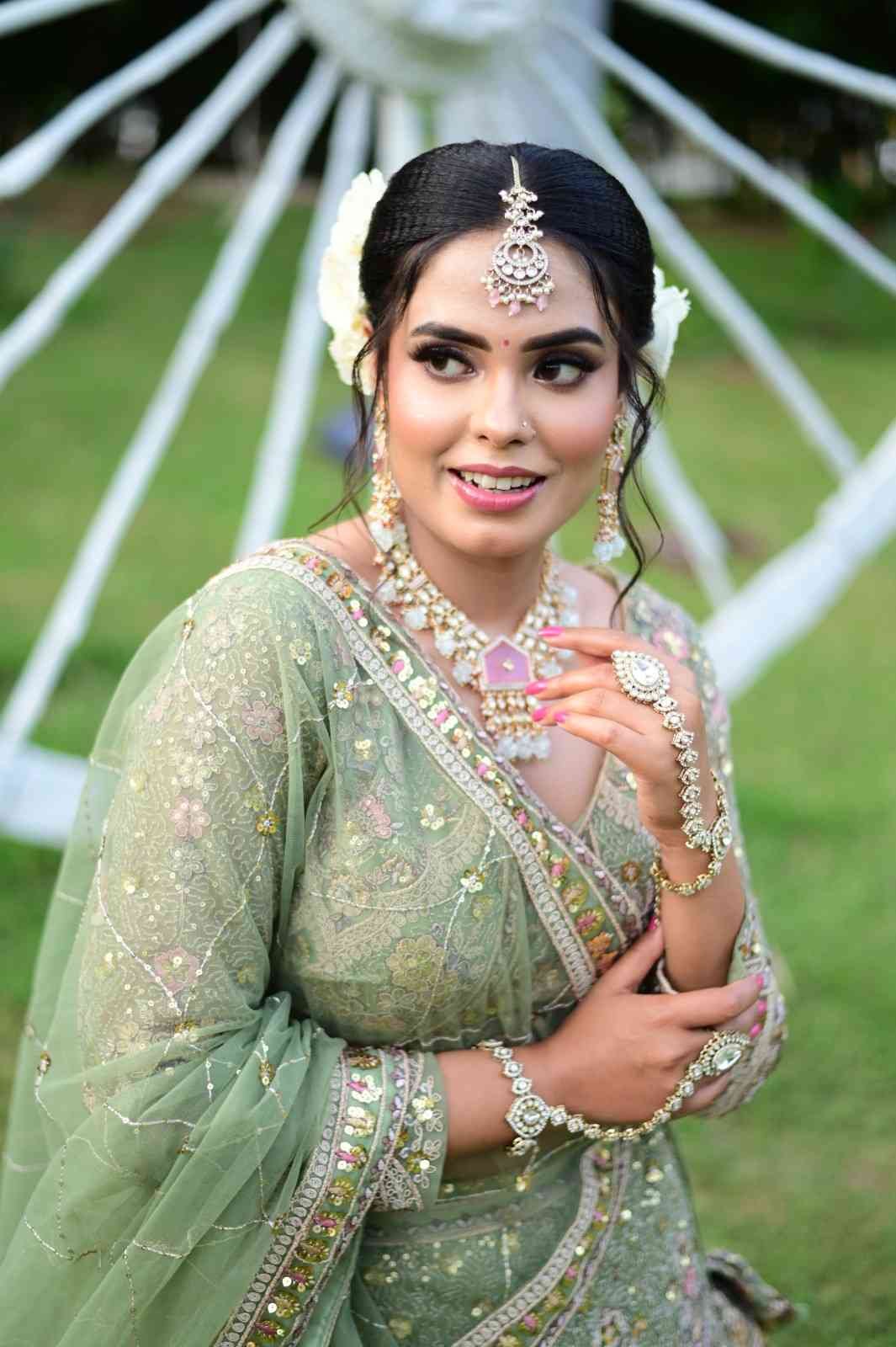 Bride in a sage green lehenga with a floral hair accessory, posed outdoors
