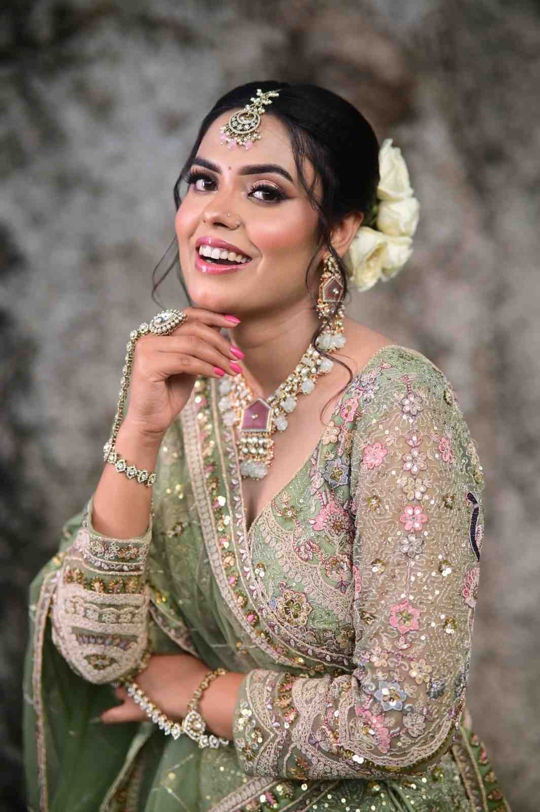 Smiling bride in a sage green embroidered lehenga with white flowers in her hair