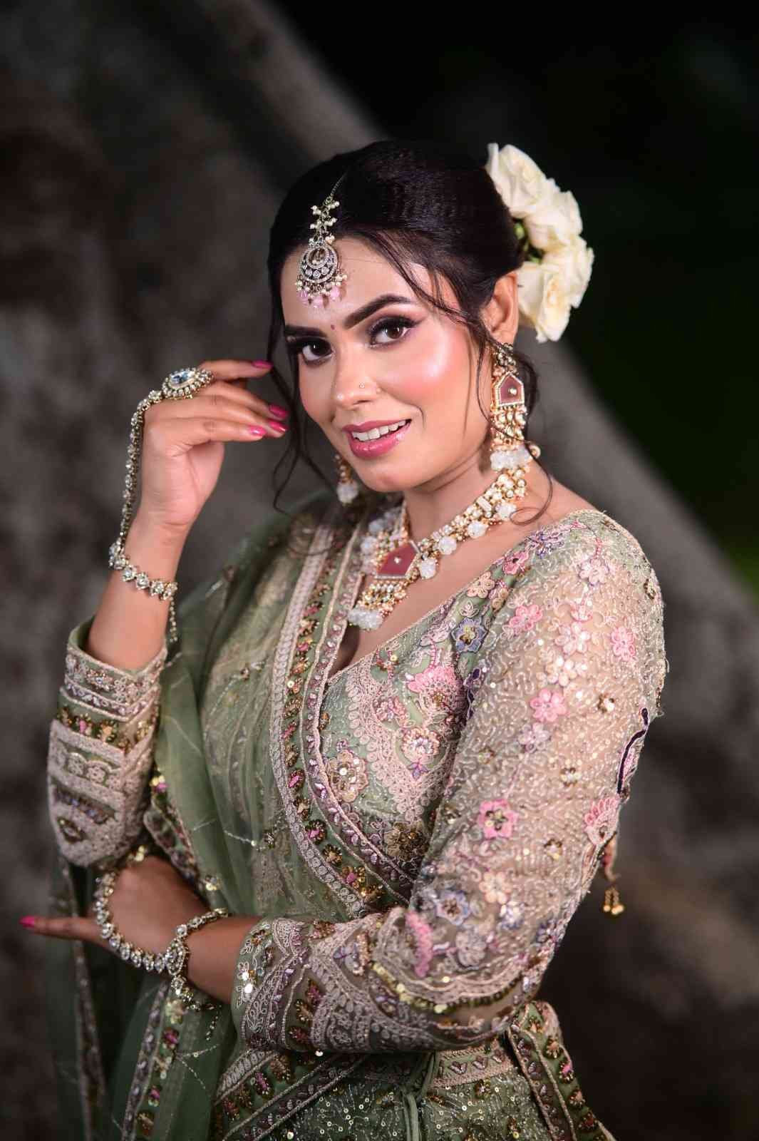 Bride in a sage green lehenga with a floral hair accessory and kundan jewellery