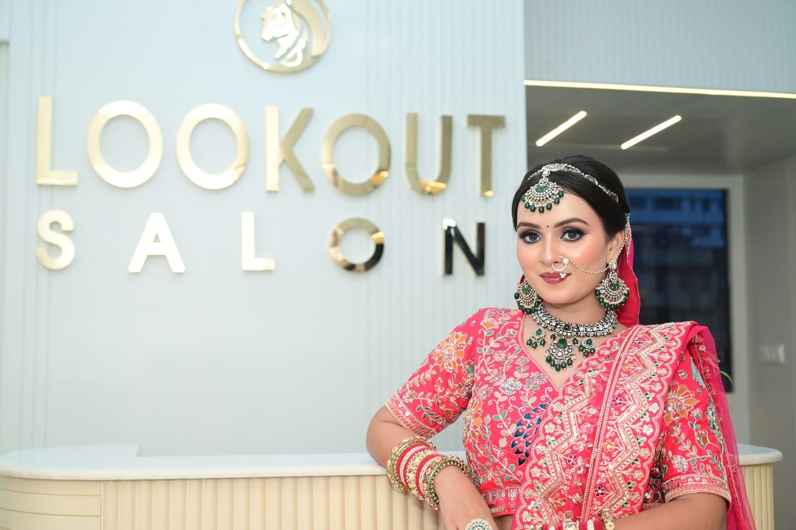 Bride in a red embroidered lehenga with kundan jewellery, seated in front of the LookOut Salon lettering