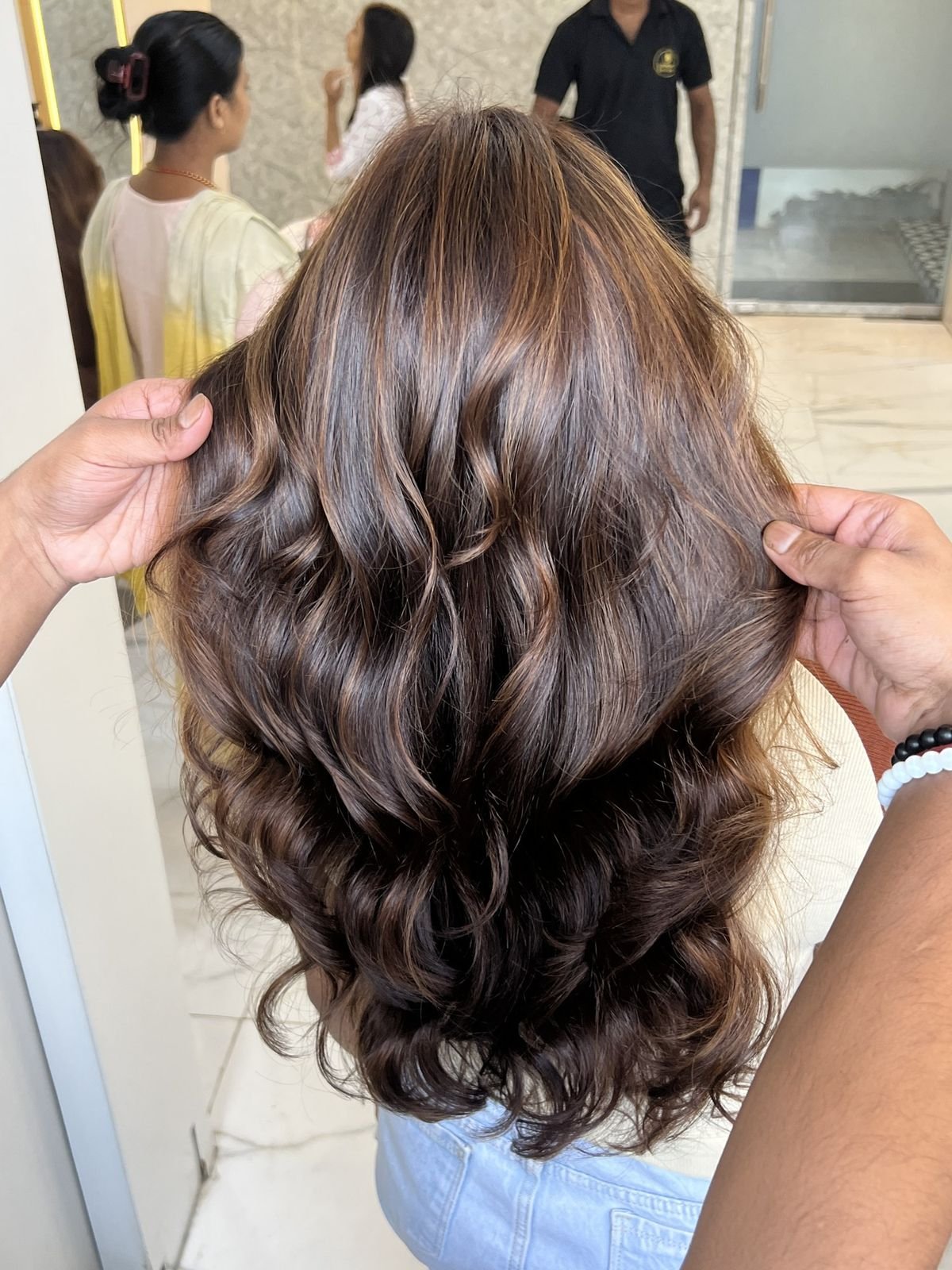 Long brown hair with volume and loose curls, held by two stylists