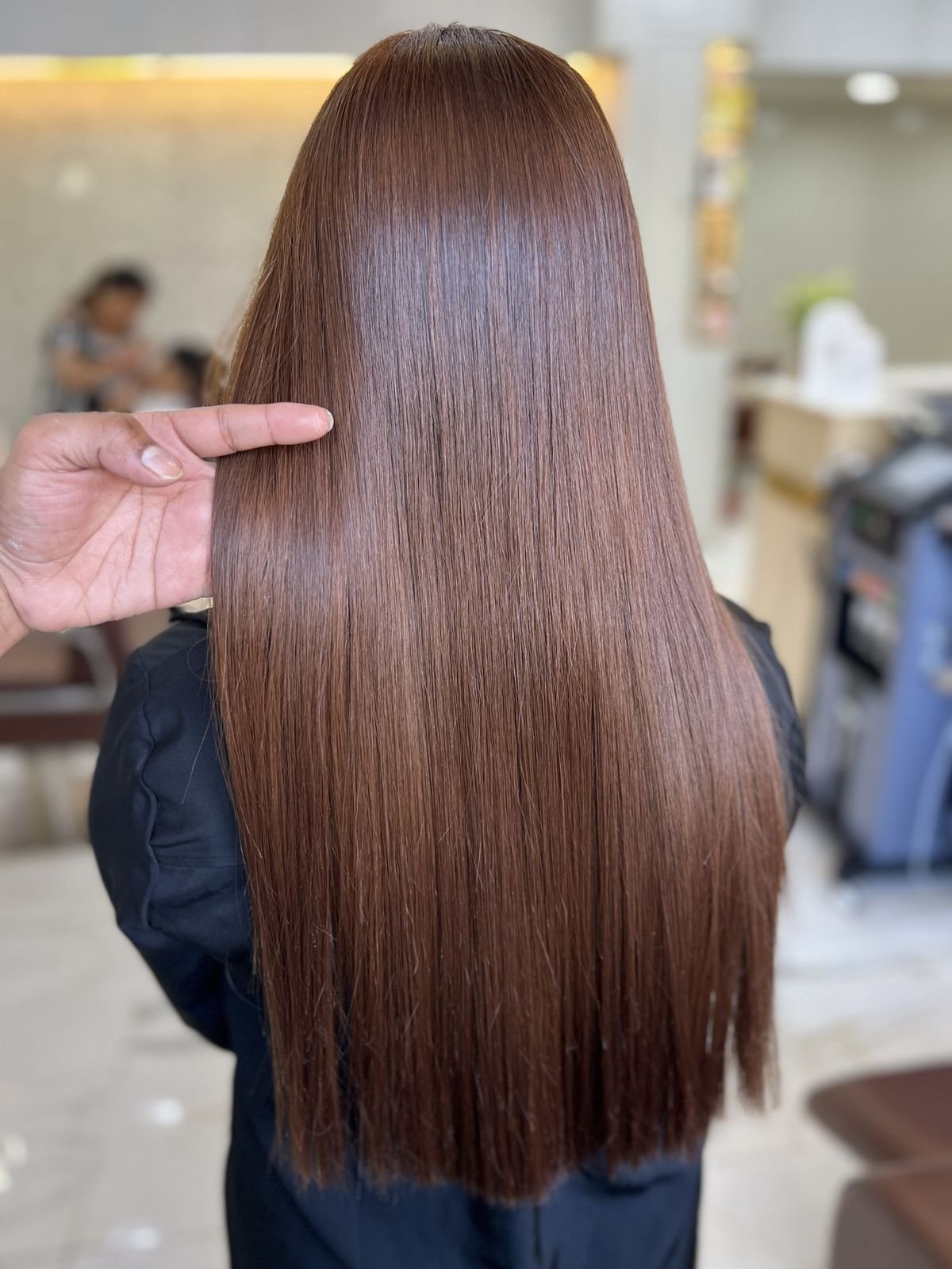 Long, silky straight brown hair held out by a stylist