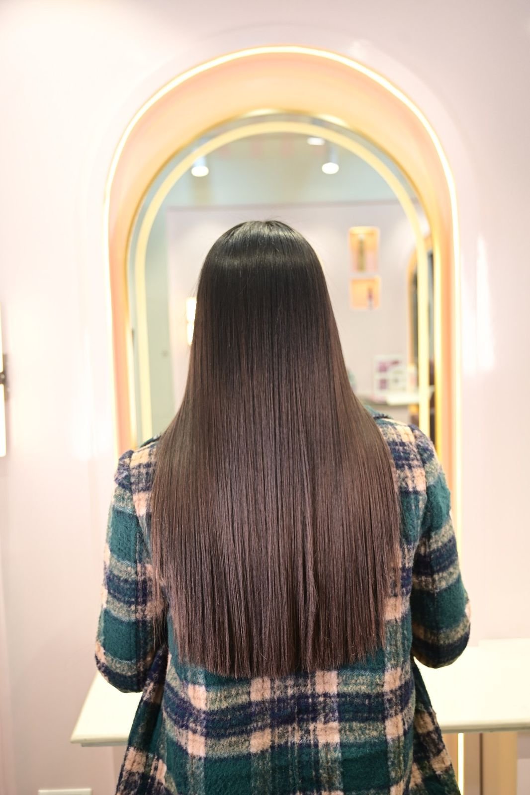 Back view of long, straight dark hair in front of an arched gold-framed mirror