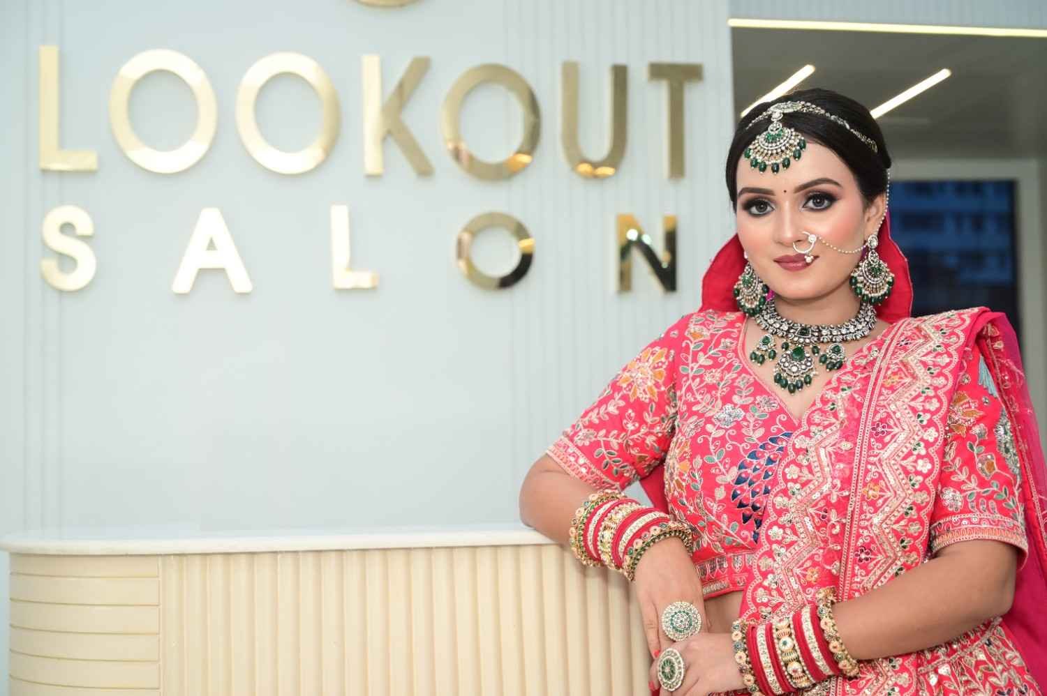 Bride in a pink embroidered lehenga with green kundan jewellery, standing in front of the LookOut Salon gold lettering
