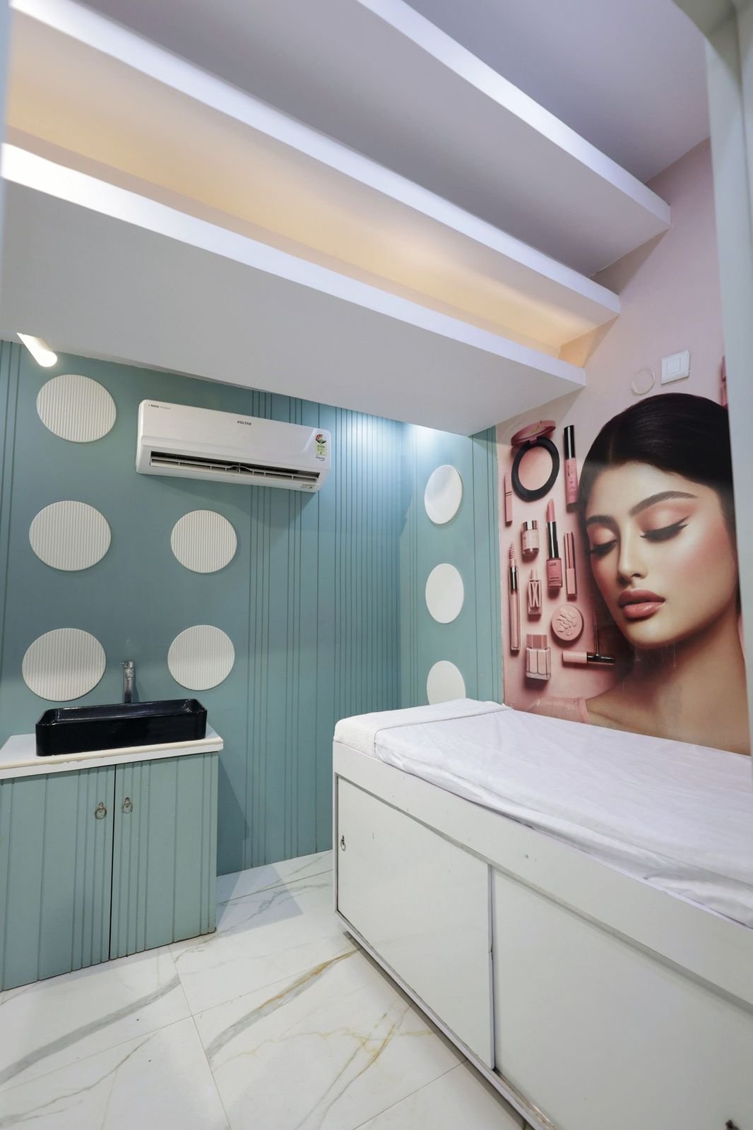 Treatment room with a bed, wall-mounted artwork of a woman and a pale blue panelled wall