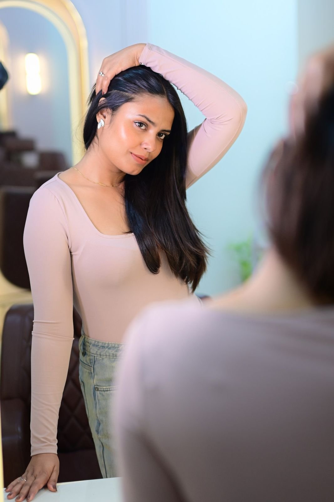 Woman with long dark hair posing beside an arched gold-framed mirror in the salon