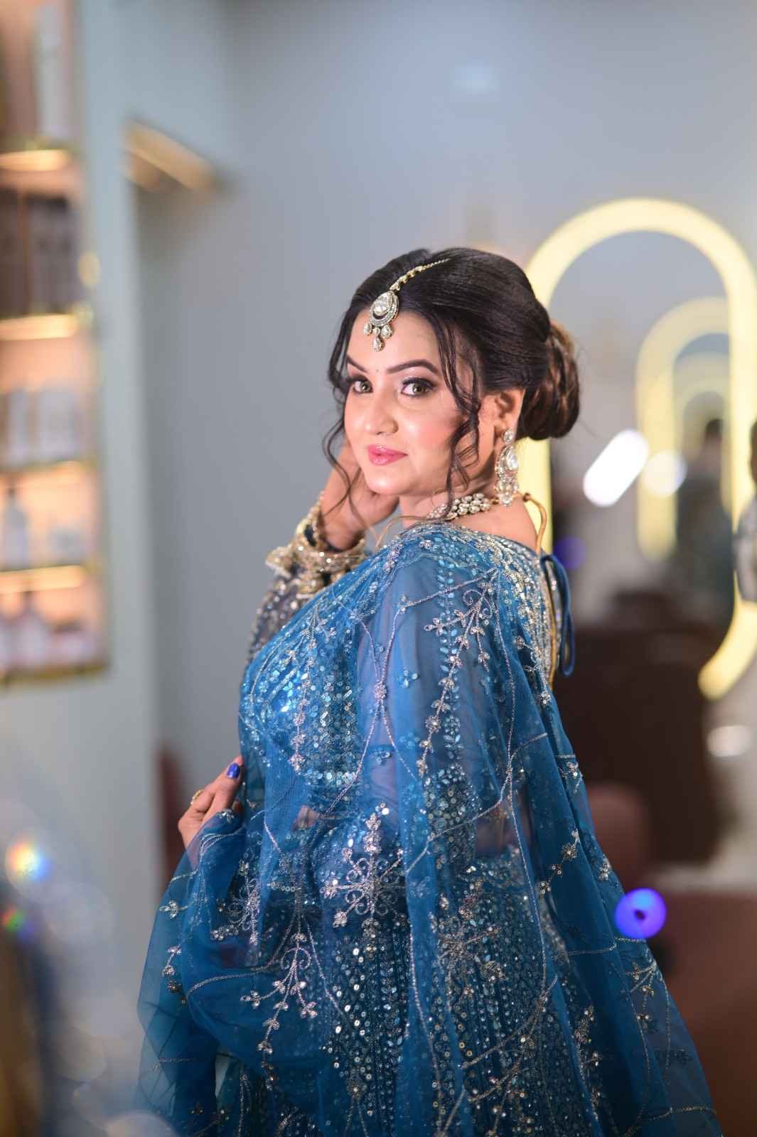 Woman in a blue embellished lehenga with a maang tikka standing inside the salon