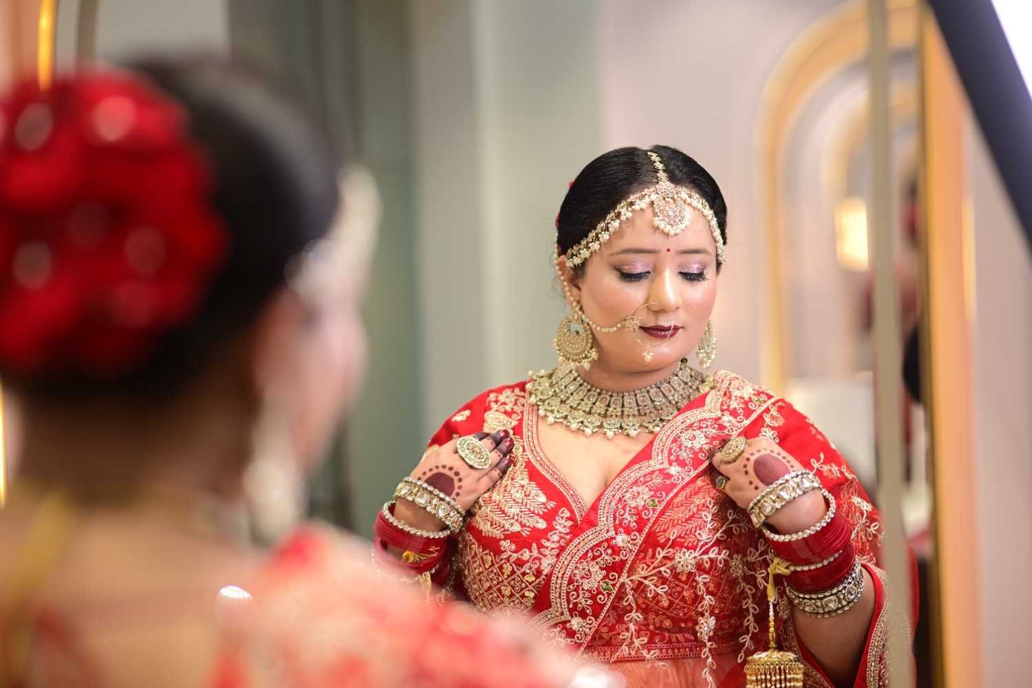 Bride in red bridal wear with gold jewellery, seen in a mirror inside the salon