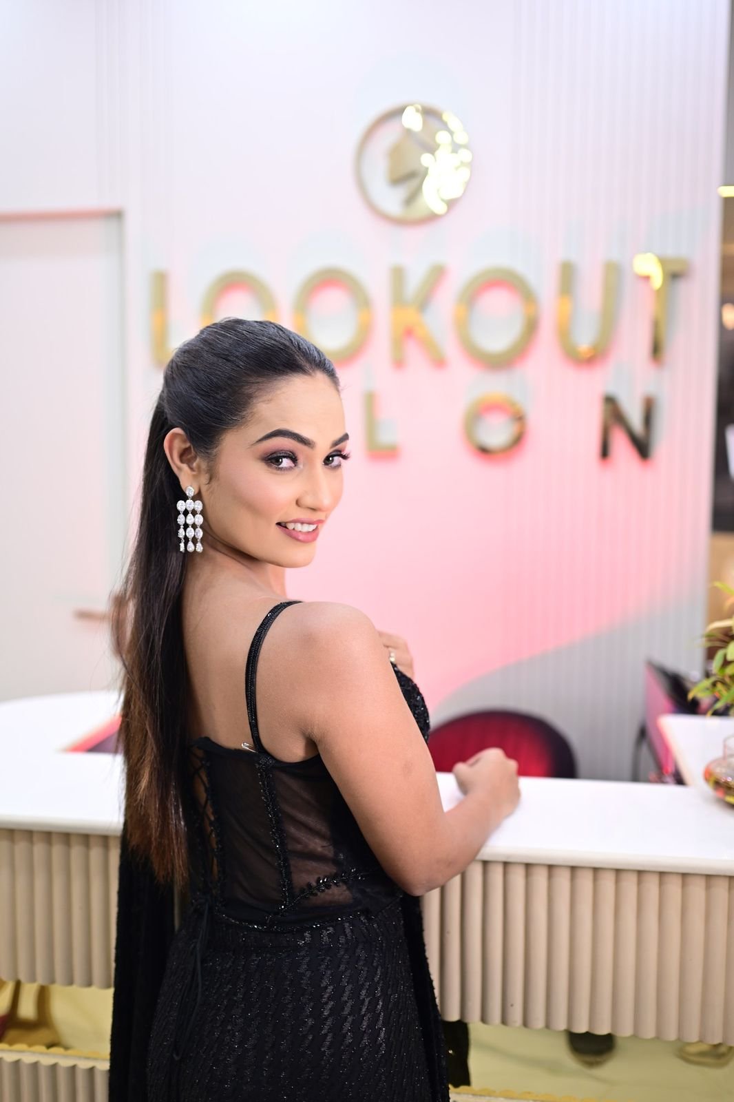 Woman with a high ponytail and drop earrings, standing at the LookOut Salon reception